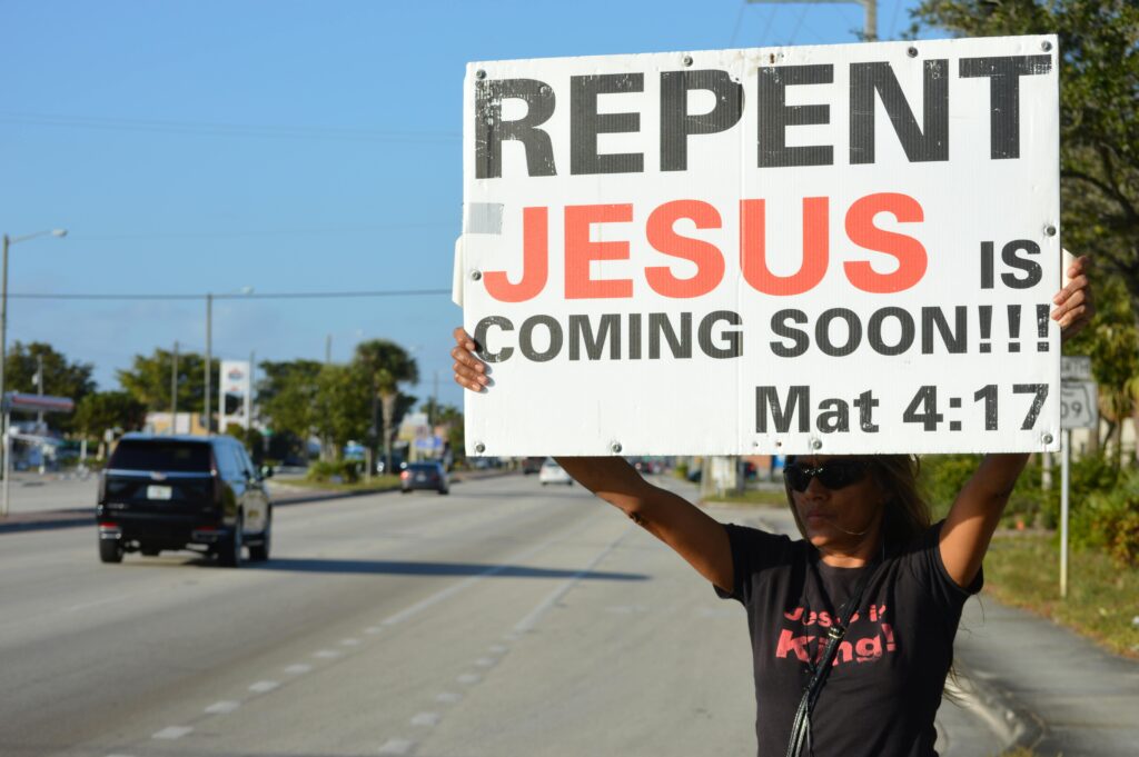 Woman holding a religious billboard on a street, emphasizing faith and repentance.