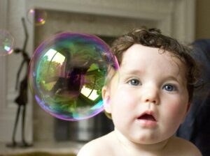 Cute baby looking at a large colorful bubble indoors with curiosity and joy.