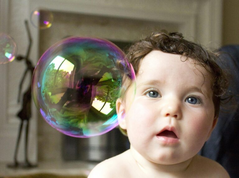 Cute baby looking at a large colorful bubble indoors with curiosity and joy.