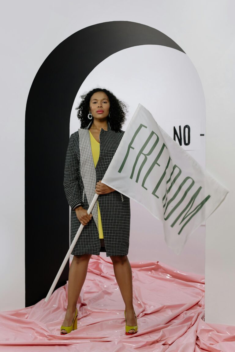 Confident woman in stylish outfit holds 'freedom' flag indoors, symbolizing empowerment.