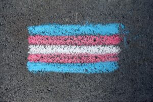 Close-up of a transgender pride flag chalk drawing on rough pavement surface.