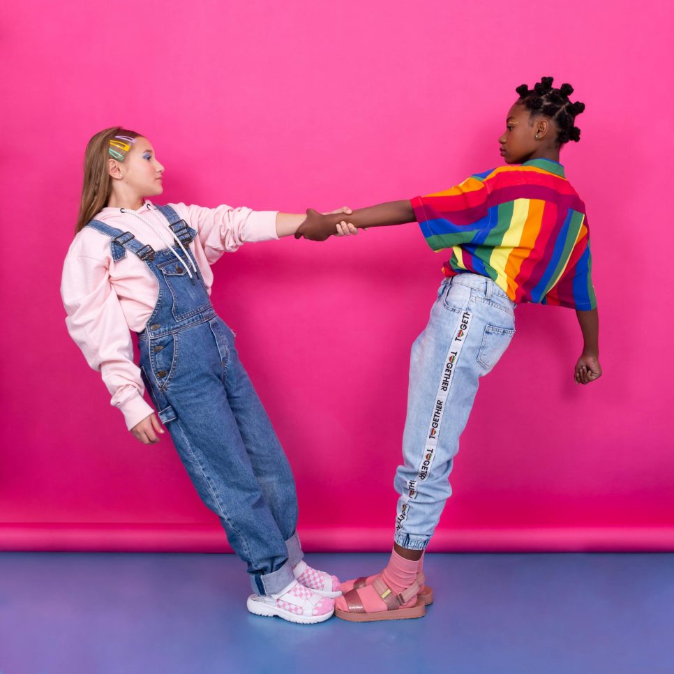 Two girls holding hands against a vibrant pink background, showcasing friendship and diversity.