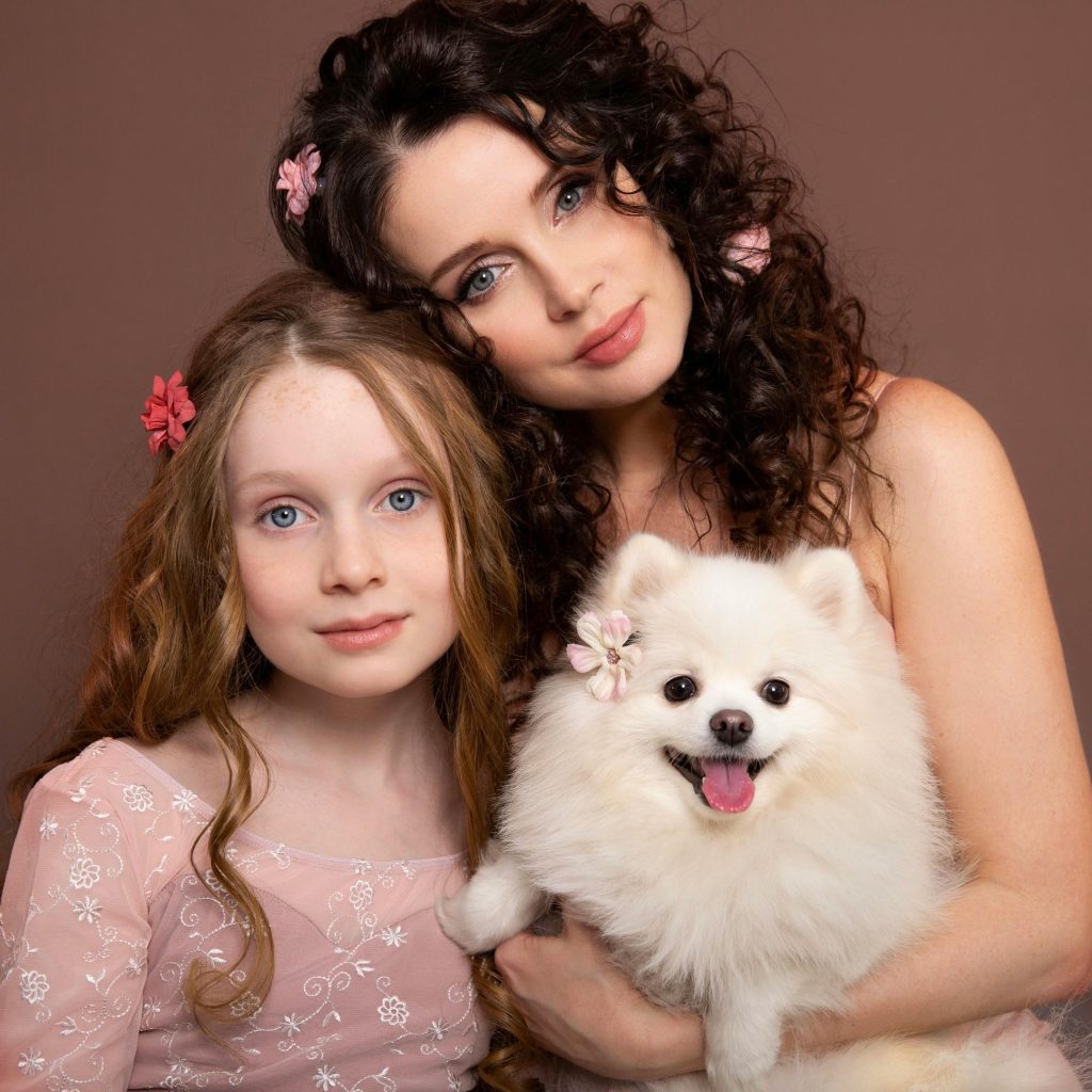 A loving portrait of a mother, daughter, and their fluffy white Pomeranian dog.