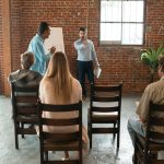 A group of adults attending an indoor workshop with a brick-wall backdrop.