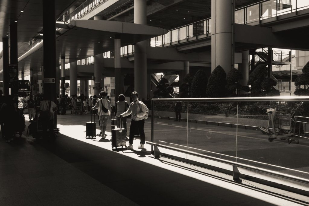 Silhouettes of travelers with luggage at a sunlit modern airport terminal.